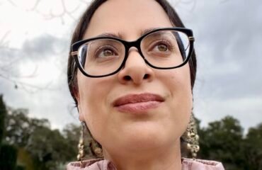 A woman with glasses in a pink top looks off camera