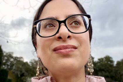 A woman with glasses in a pink top looks off camera