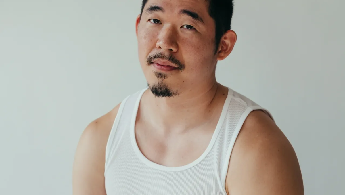 Asian American man (poet Jimin Seo) looks at camera, wearing a white A T-Shirt and black pants