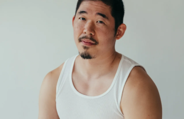 Asian American man (poet Jimin Seo) looks at camera, wearing a white A T-Shirt and black pants