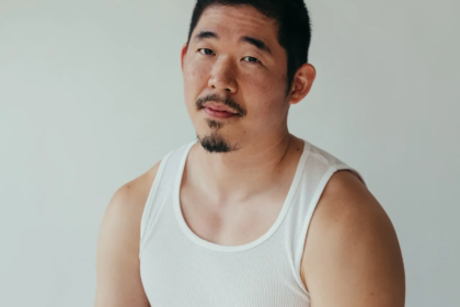 Asian American man (poet Jimin Seo) looks at camera, wearing a white A T-Shirt and black pants