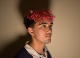 Poet with pink hair looks off camera.
