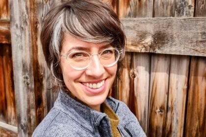 Stefanie Kirby Headshot Brunette woman (Stefanie Kirby) with short hair and a blue shirt grins at camera.