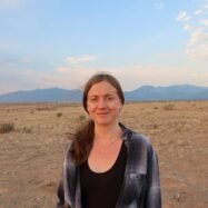 Woman (Jill Kitchen) stands with mountains in background.