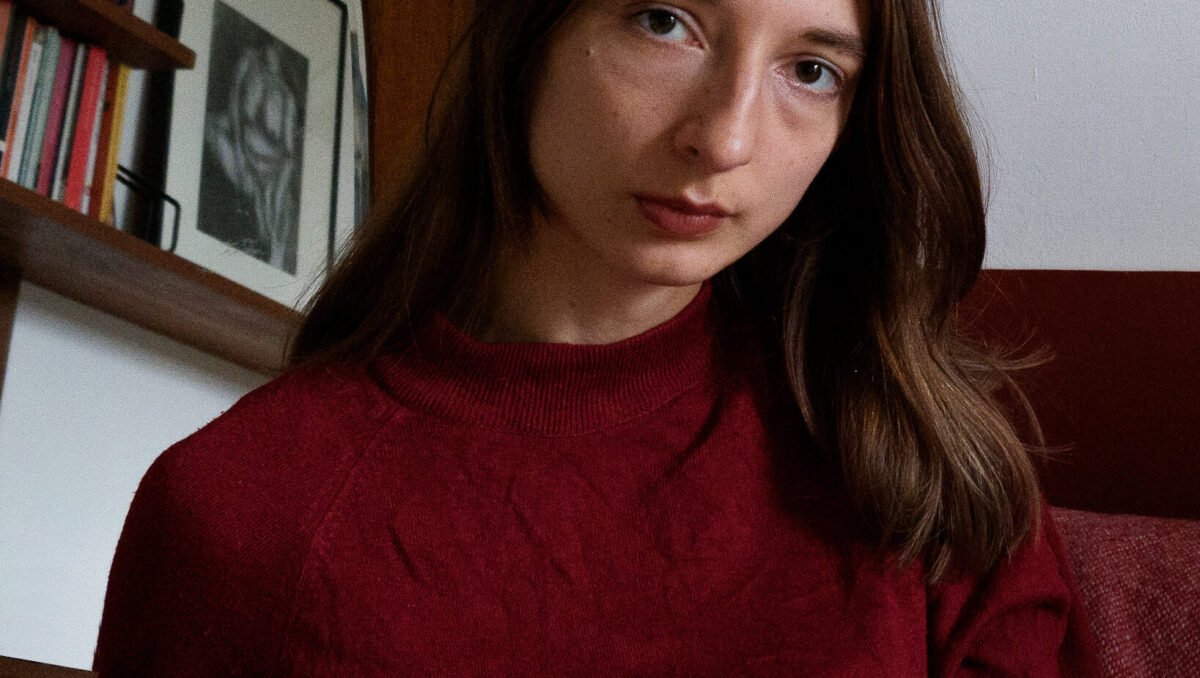 Brunette woman (Nasim Luczaj) in red top looks at camera.