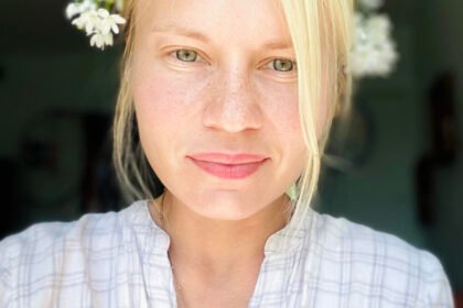Blonde woman with flowers in her hair (Zakharkiv) looks at the camera.