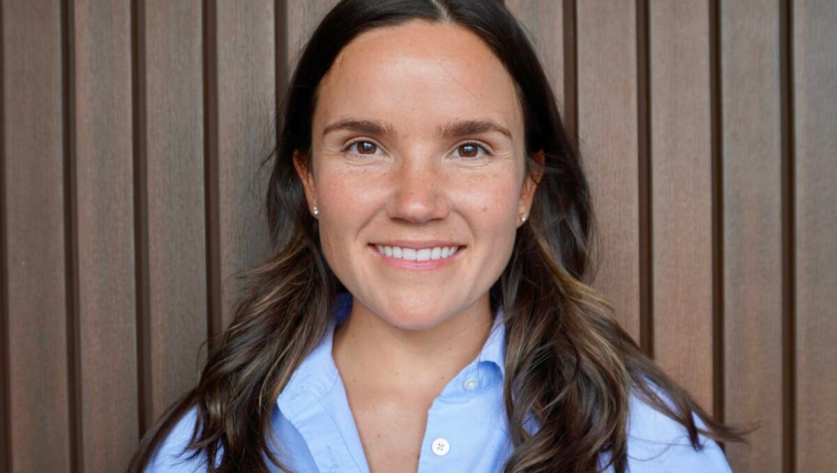 Portrait of woman with brown hair, in a blue collared shirt, smiling at the camera.