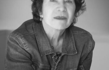 Black and white photo of a woman with short, dark curly hair, staring into the camera.