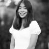 Black and white photo of an Asian woman in white top, smiling at camera.