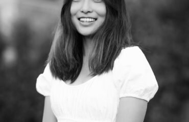 Black and white photo of an Asian woman in white top, smiling at camera.
