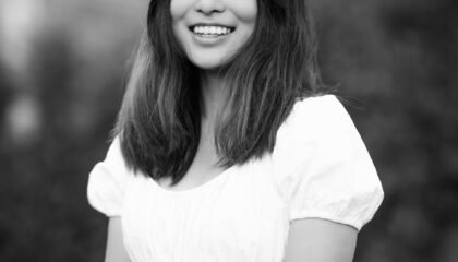 Black and white photo of an Asian woman in white top, smiling at camera.