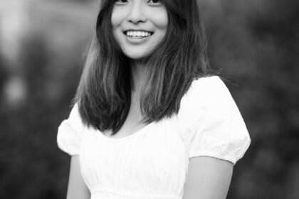 Black and white photo of an Asian woman in white top, smiling at camera.