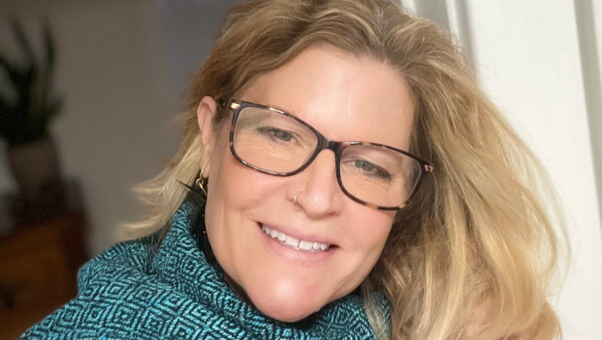 Kim Jan 2025 Blonde woman in blue turtleneck smiles into the camera.