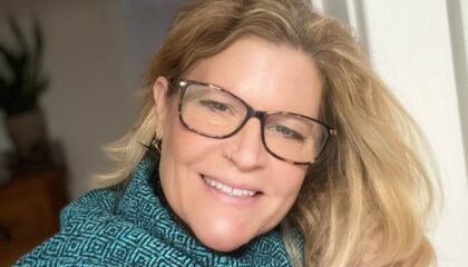 Blonde woman in blue turtleneck smiles into the camera.