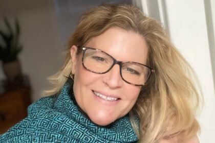 Blonde woman in blue turtleneck smiles into the camera.