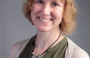 Woman in green top and white cardigan smiles at camera.