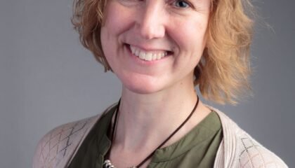 Woman in green top and white cardigan smiles at camera.