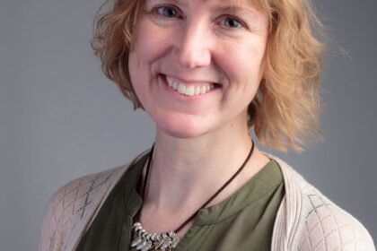 Woman in green top and white cardigan smiles at camera.