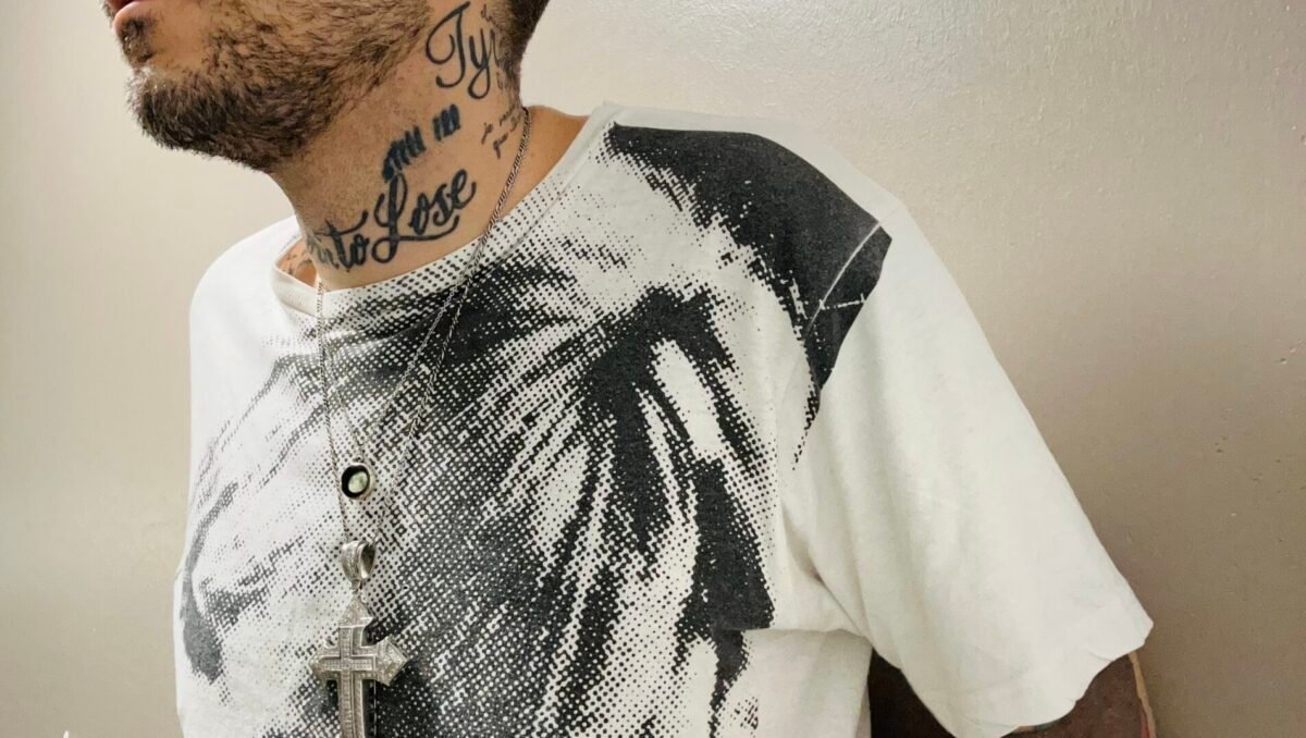 Tattooed man in black and white Velvet Underground shirt looks off camera.