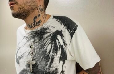 Tattooed man in black and white Velvet Underground shirt looks off camera.