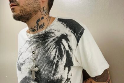 Tattooed man in black and white Velvet Underground shirt looks off camera.