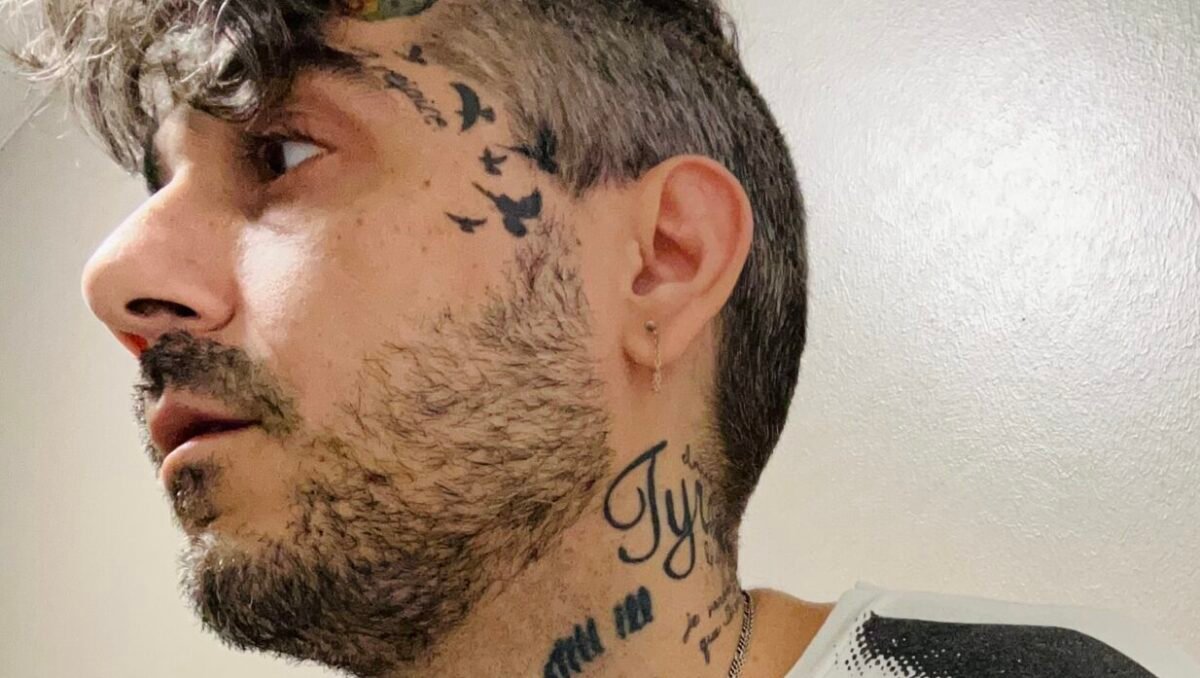 Tattooed man in black and white Velvet Underground shirt looks off camera.