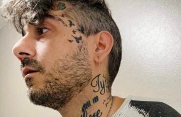 Anthony Thomas Lombardi Tattooed man in black and white Velvet Underground shirt looks off camera.