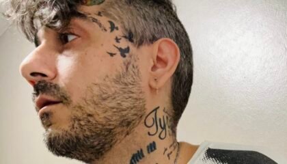 Tattooed man in black and white Velvet Underground shirt looks off camera.