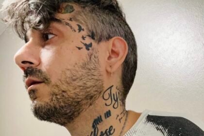 Tattooed man in black and white Velvet Underground shirt looks off camera.