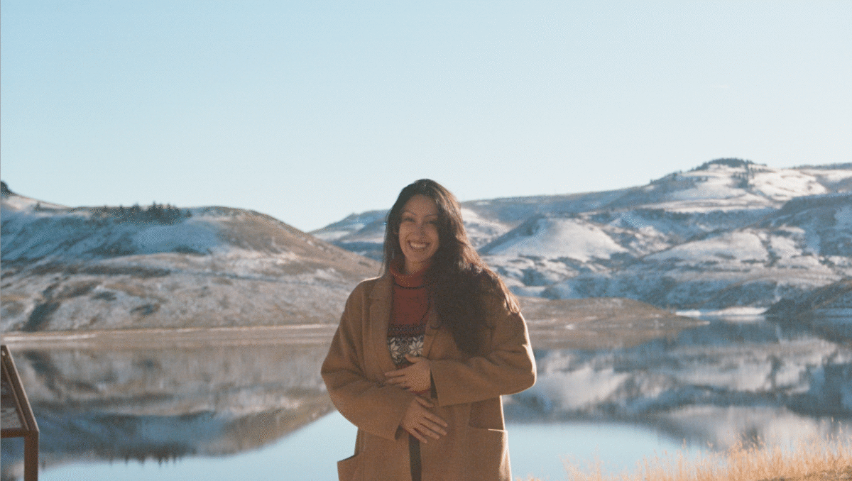 Gabriela Valencia Woman in tan jacket stands in front of mountains and lake.