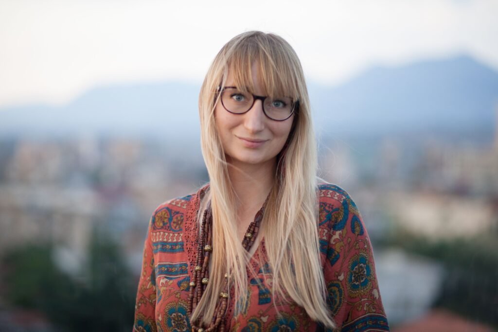 Woman with glasses and bangs looks at the camera, smiling.