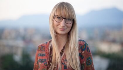 Woman with glasses and bangs looks at the camera, smiling.