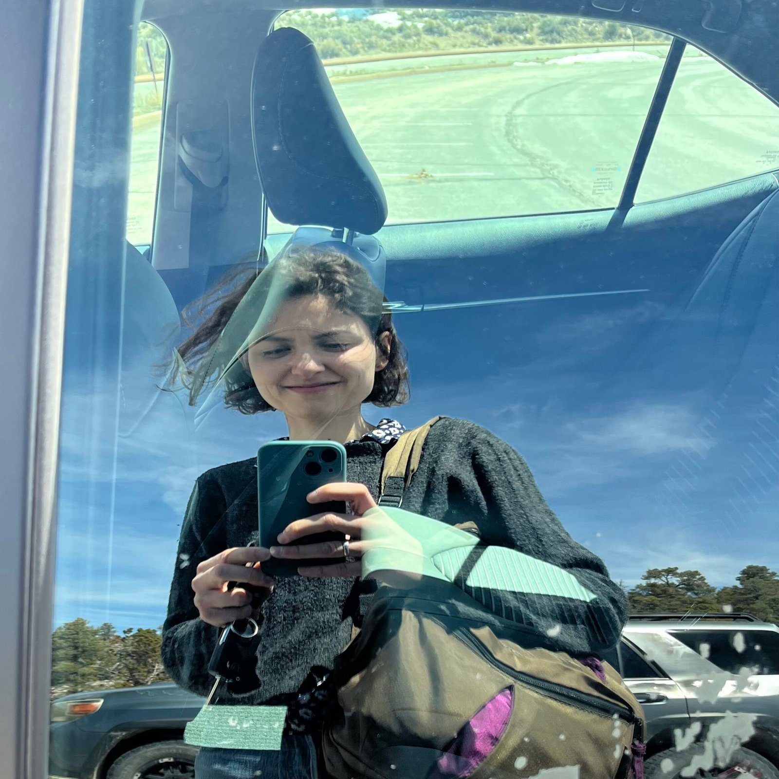 Woman with short hair takes a selfie in a car window.